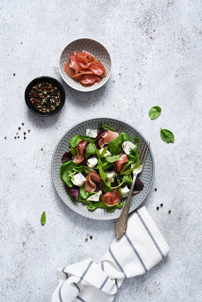 Arugula salad, chard with blue cheese and prosciutto with sauce on a concrete background, top view. - Foto, immagini