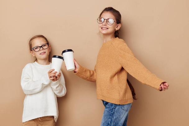 two little funny girls a glass with a drink beige background - Foto, Bild