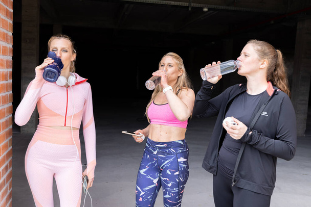 Sporty beautiful young women of different body types drinking water from bottle after working out of a gym, gym, fitness, sport concept  - Фото, изображение