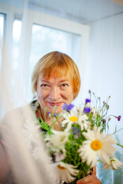 Elderly woman with   bouquet of live wildflowers in   home interior. - Fotoğraf, Görsel