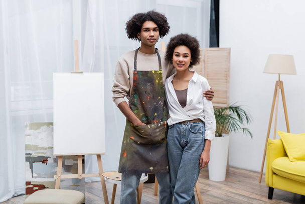 Young african american couple smiling at camera near easel at home  - Foto, Bild