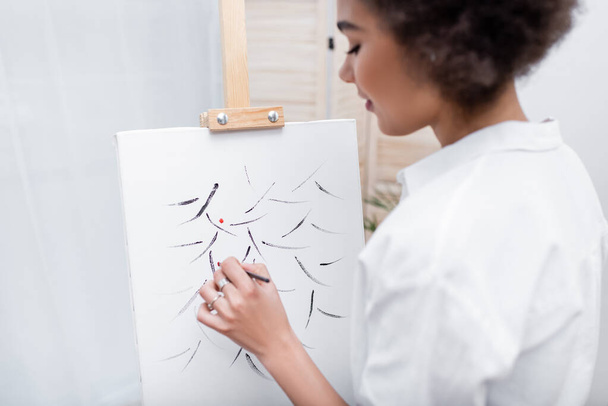 Side view of young african american woman painting on canvas at home  - 写真・画像