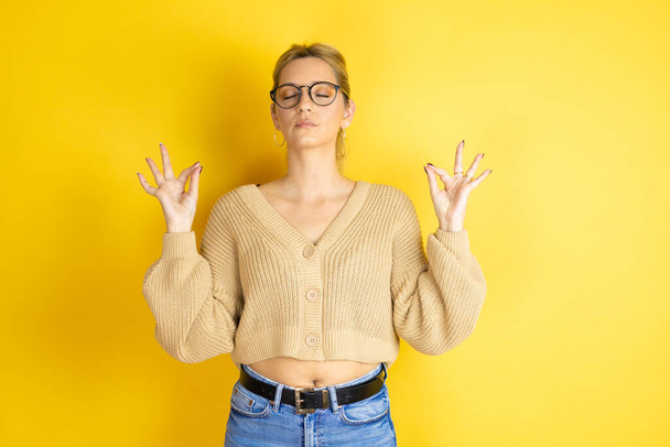 Young beautiful woman wearing casual sweater over isolated yellow background relax and smiling with eyes closed doing meditation gesture with fingers - Zdjęcie, obraz