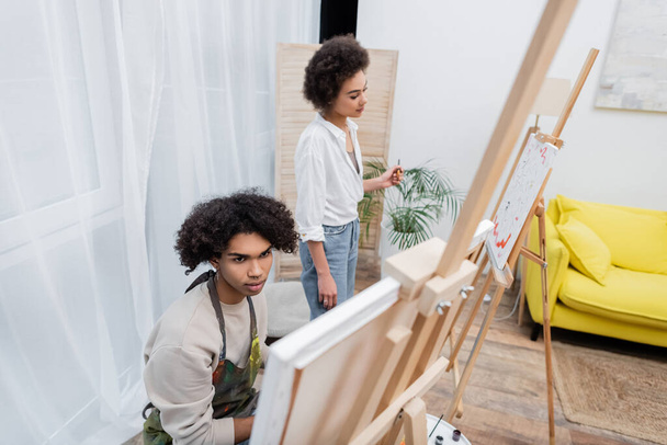 Young african american couple looking at canvases on easels at home  - Photo, Image
