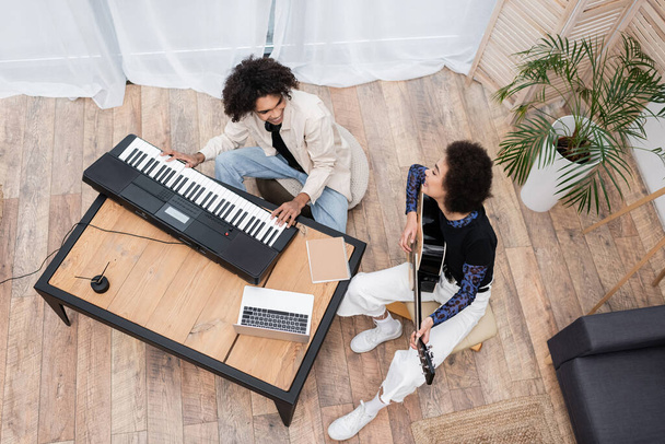 Overhead view of smiling african american couple playing musical instruments near laptop at home  - Photo, Image