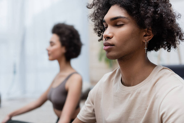 Young african american man meditating near blurred girlfriend at home  - Foto, Imagem