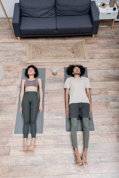 Top view of african american couple lying on yoga mats in living room  - Photo, Image