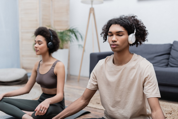 Afroamerikaner meditiert mit Kopfhörern in der Nähe seiner Freundin zu Hause  - Foto, Bild