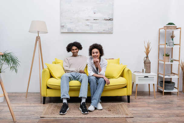 Smiling african american woman looking at camera near boyfriend on couch at home  - Foto, Bild