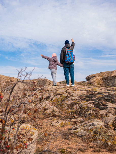 Travelers father daughter with raised hands walking climbing on mountain summit enjoying aerial view blue cloudy sky back view together. Active Lifestyle Family Travel Scenic landscape hiking Backpack - Photo, Image