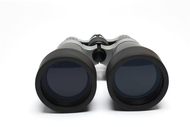 Primer plano de las dos lentes delanteras de un gran campo binocular negro y gris sobre un fondo blanco como concepto para el espionaje y la observación a través de la visión - Foto, Imagen