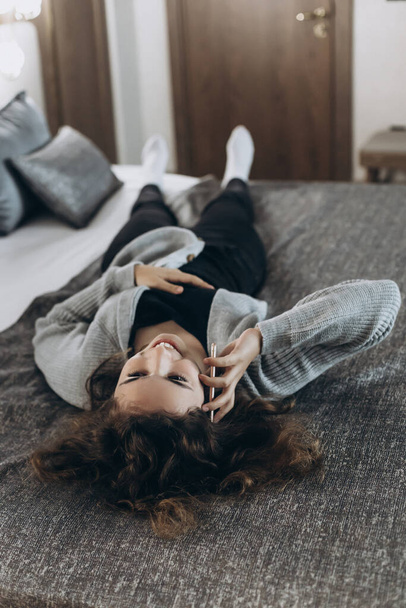 Щаслива усміхнена дівчина-підліток розмовляє по телефону лежачи на спині на ліжку
 - Фото, зображення