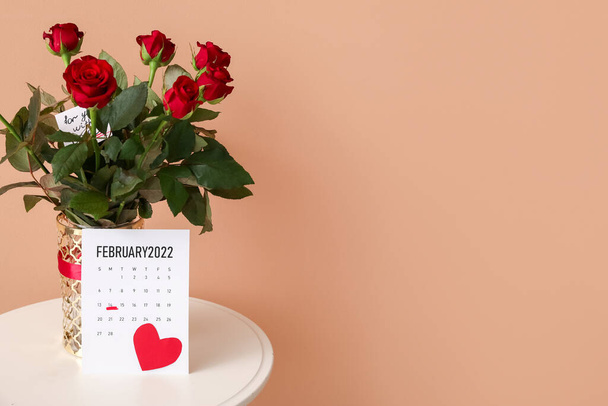 Ramo de flores y calendario con fecha marcada del Día de San Valentín en la mesa sobre fondo de color - Foto, Imagen