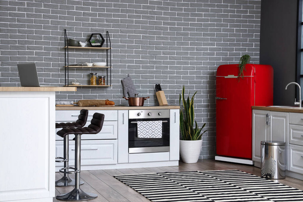 Interior de cozinha elegante com geladeira vermelha, balcões brancos e parede de tijolo - Foto, Imagem