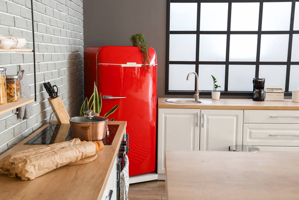 Інтер'єр стильної кухні з червоним холодильником, білими лічильниками і вікном
 - Фото, зображення
