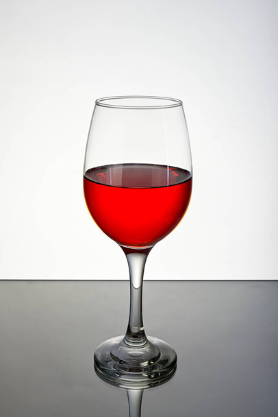 Glas rode wijn, op een reflecterend oppervlak met een witte achtergrond. - Foto, afbeelding