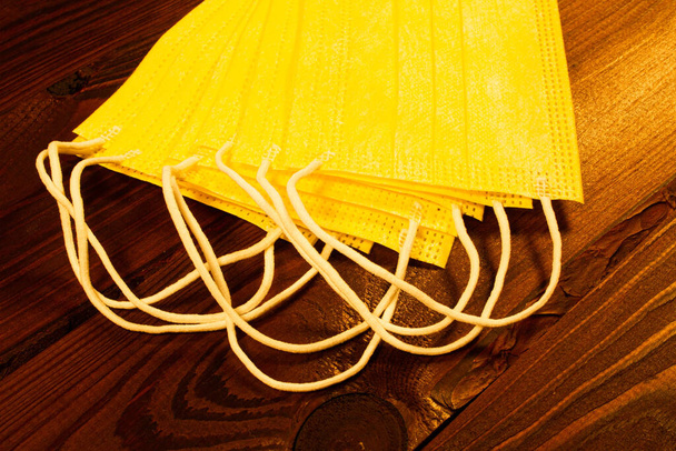 Yellow medical disposable face masks on a brown wooden table. Lots of surgical 3 ply masks on a beautiful wooden textured background. Hygiene and health. Protection against a new strain of coronavirus - Photo, Image