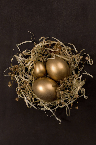 Pozdrav se zlatými velikonočními vejci v hnízdě na černém pozadí. Horní pohled - Fotografie, Obrázek