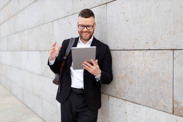 Веселий бізнесмен на веб-камеру планшета під час онлайн-зустрічі, стоячи зовні під бетонною стіною
 - Фото, зображення