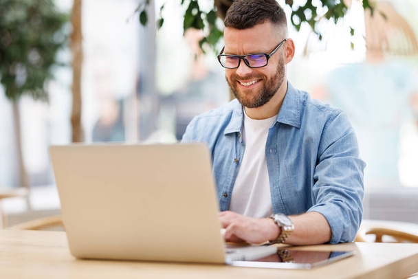 Ευτυχισμένος νεαρός άνδρας επιχειρηματίας που κάθεται μπροστά από το φορητό υπολογιστή έξω από την εργασία και έχουν τηλεδιάσκεψη σε απευθείας σύνδεση - Φωτογραφία, εικόνα