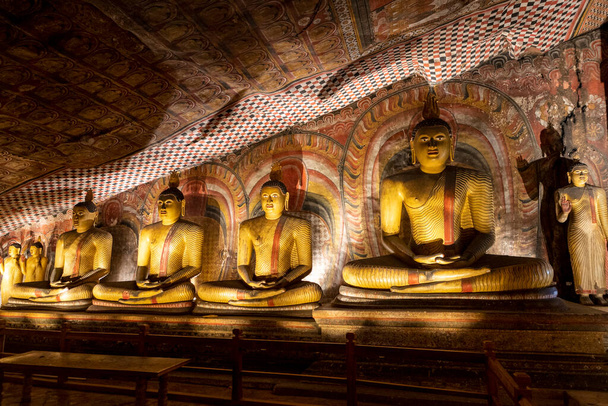 Sri Lanka. Dambulla Cave Temple. Buddha statues sitting in a row, illuminated by lamps from below. - Fotó, kép