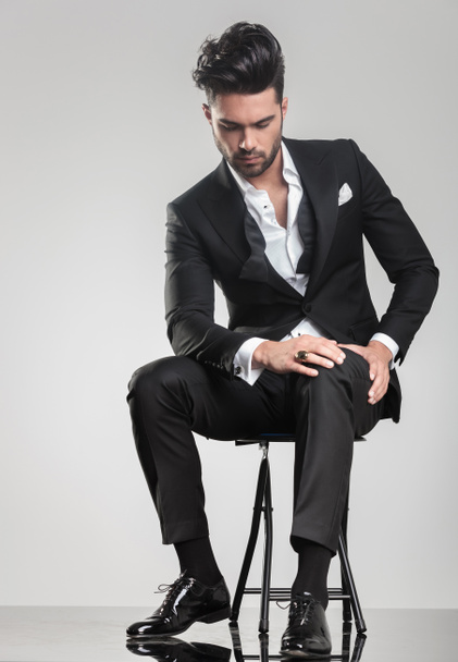Elegant young man stitting on a stool while looking down - Foto, immagini