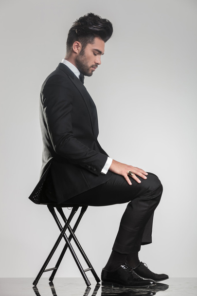елегантний молодий чоловік сидить на табуреті, дивлячись вниз
 - Фото, зображення