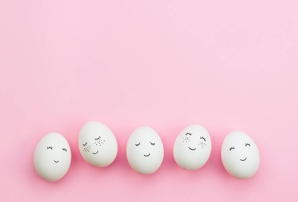 Πασχαλινά αυγά με χαριτωμένα πρόσωπα ζωγραφισμένα σε ένα λεπτό ροζ φόντο. Η έννοια των διακοπών του Πάσχα. Πάνω όψη, αντιγραφή χώρου. - Φωτογραφία, εικόνα