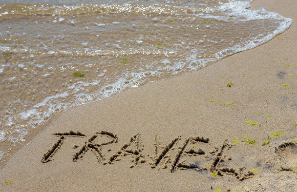 Matkakonsepti - kirjoitus hiekkaan. Meren hiekkaranta. Motivaatiota. Valtameren aalto. Sana matkustaminen on kirjoitettu meren rannalla. Lomat rannalla. - Valokuva, kuva