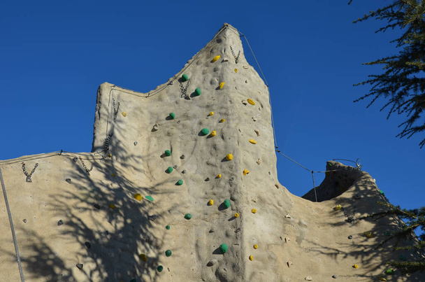 自然の形の人工石で作られたクライミングウォール不規則な間隔とねじ石。ロープの上の登山者を確保するためにハンドルやバックル、キャビナー、ハンギングや使用 - 写真・画像