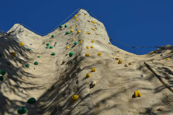 pared de escalada hecha de piedra artificial de formas naturales con piedras irregulares espaciadas y atornilladas. manijas y hebillas, mosquetones, colgados y utilizados para asegurar a los escaladores en la cuerda - Foto, imagen