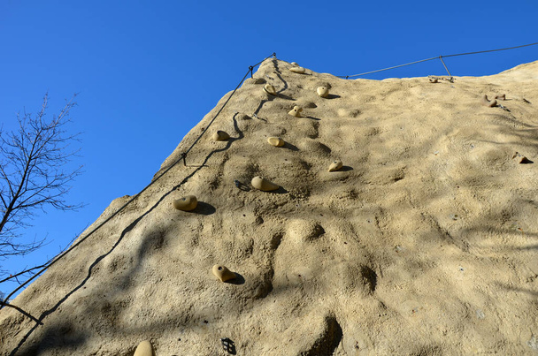 mur d'escalade en pierre artificielle de formes naturelles avec des pierres irrégulièrement espacées et vissées. poignées et boucles, mousquetons, suspendus et utilisés pour fixer les grimpeurs sur la corde - Photo, image