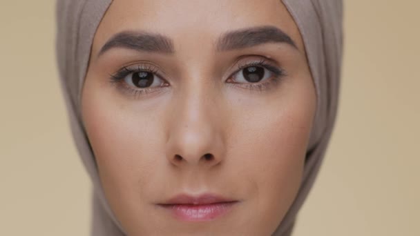 Primer plano retrato de una joven árabe seria mujer islámica con pañuelo tradicional mirando a la cámara y parpadeando - Imágenes, Vídeo