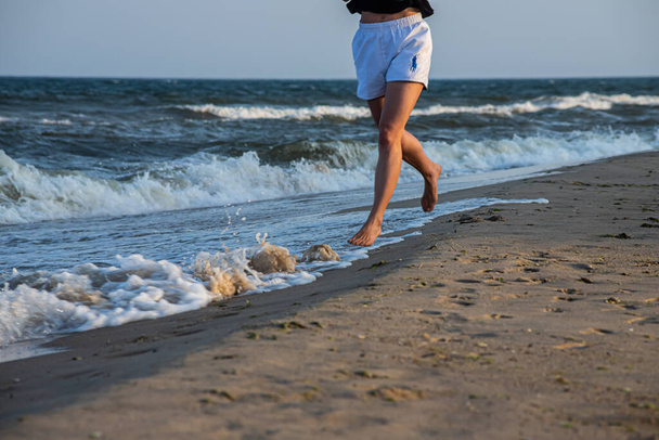 Woman is running ahead on beach of sea. Legs close-up. - Valokuva, kuva