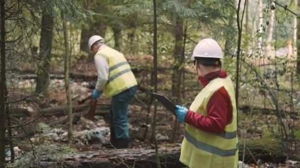 Эколог в рабочей одежде и шлеме чистый пластиковый мусор в лесу - Кадры, видео