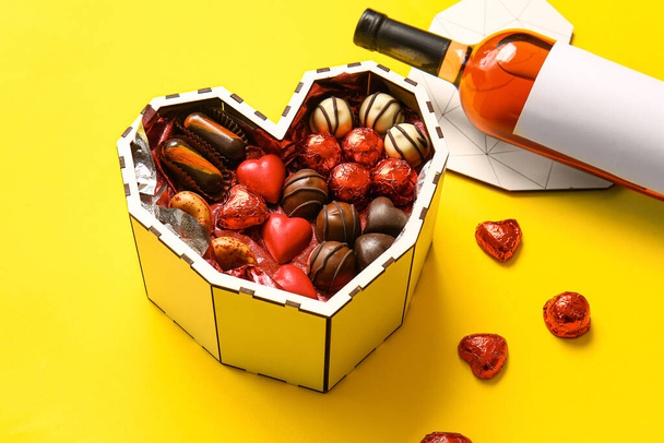 Heart shaped box with tasty chocolate candies on yellow background - Foto, Imagen