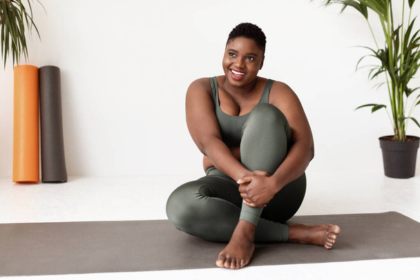 Positiva señora afroamericana más tamaño sentado en la esterilla de yoga - Foto, imagen