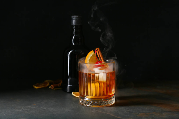 Vaso de sabroso cóctel y botella Old Fashioned con whisky sobre fondo negro - Foto, imagen