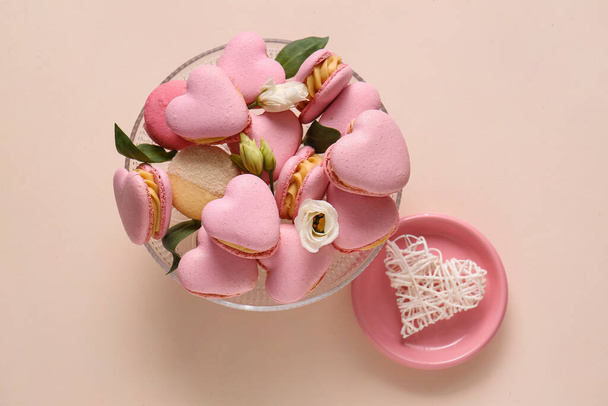 Dessert stand with tasty heart-shaped macaroons and flowers on beige background - Foto, imagen
