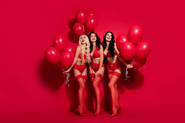 Full length body size view of three lovely cheery amazed girls holding helium balls store opening isolated on shine red color background - Foto, Imagem