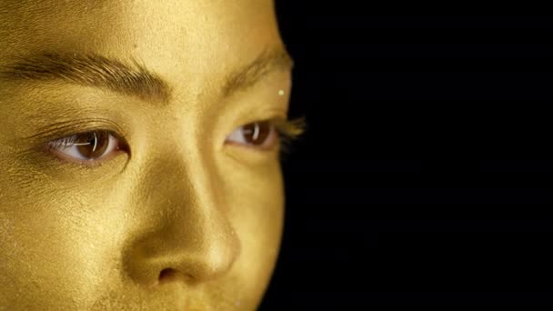 Γυναίκα με το χρυσό δέρμα κοιτάζοντας πέρα από το μαύρο φόντο, περικοπεί - Πλάνα, βίντεο