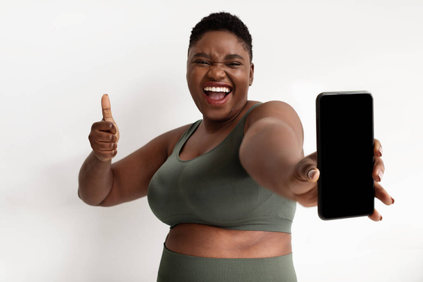 Positive sporty african american plus size woman showing cellphone, mockup - Фото, изображение