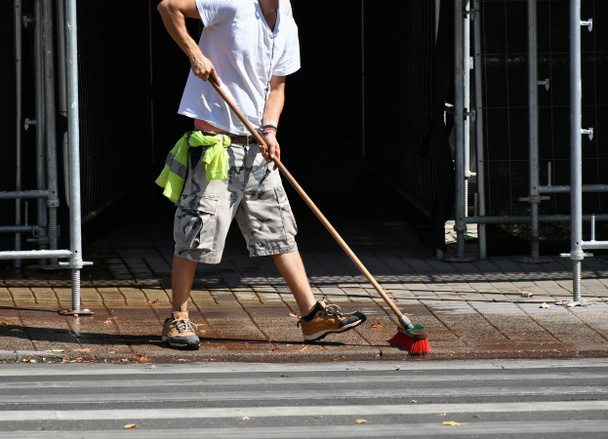 男はほうきで通りを掃除してる - 写真・画像