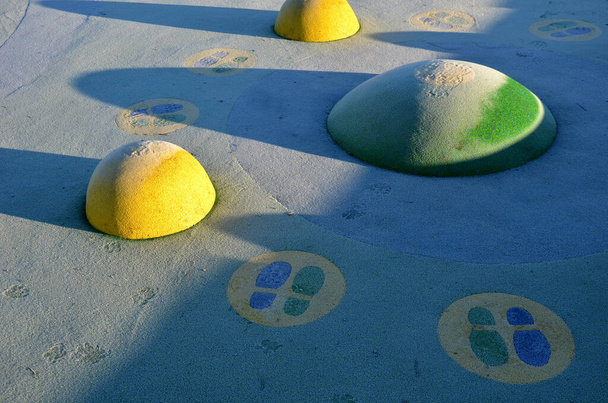 superficie in gomma bianca di un parco giochi con palette gialle e macchie colorate nel gelo delle impronte umane. lenti sollevate come palle, panche in legno e trampolini circolari affondati nel terreno. - Foto, immagini