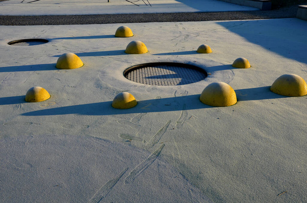 人間の足跡の霜に黄色のスクープと色の斑点の遊び場の白いゴム製の表面。ボールや木のベンチや円形のトランポリンなどの上昇レンズが地形に沈み込み. - 写真・画像