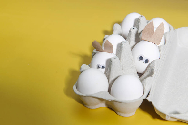 Ένα χαρούμενο λευκό αυγό με ποτήρια σε ένα κουτί με συνηθισμένα αυγά. Δημιουργική εικόνα. Έννοια Πάσχα - Φωτογραφία, εικόνα