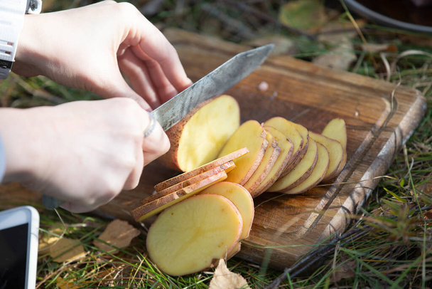 Corte de patatas para asar al aire libre. Las manos de una mujer cortan una patata con un cuchillo para una barbacoa. - Foto, imagen