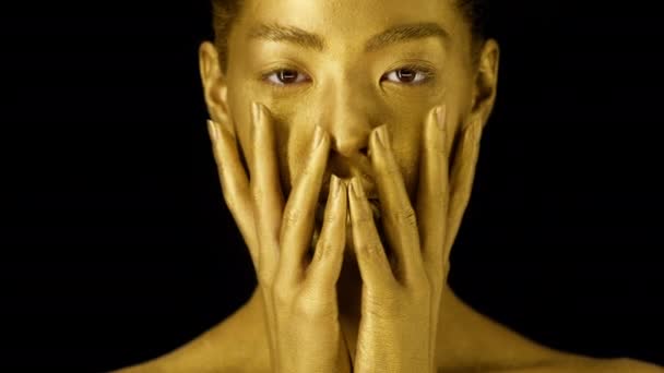 Γυναίκα με το χρυσό δέρμα αγγίζοντας το πρόσωπο πάνω από το μαύρο φόντο - Πλάνα, βίντεο