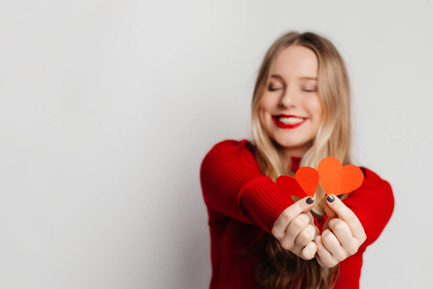 Žena držící papírová srdce, pózující na bílém pozadí studia, usmívající se do kamery. Happy Valentine's holiday celebration - Fotografie, Obrázek
