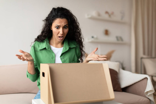Незадоволений жінка клієнт розпаковує картонну коробку вдома
 - Фото, зображення